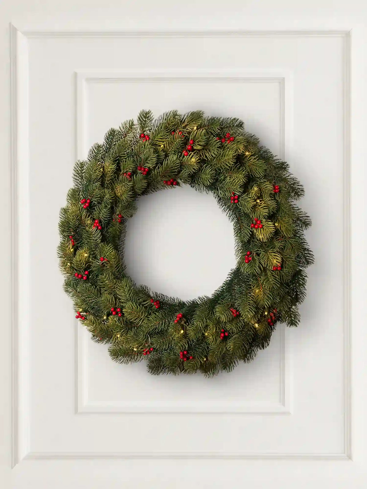 ArtiTree-kerstkrans met rode bessen en ledverlichting hangt decoratief aan een lichte muur in een gezellige woonkamer