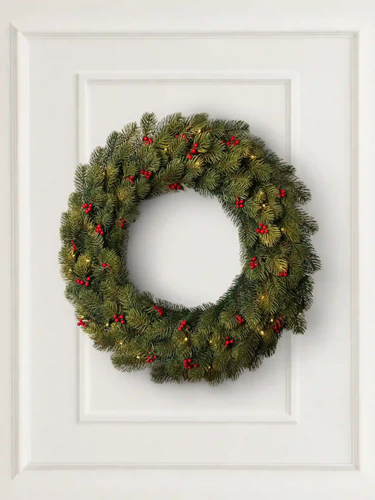ArtiTree-kerstkrans met rode bessen en ledverlichting hangt decoratief aan een lichte muur in een gezellige woonkamer